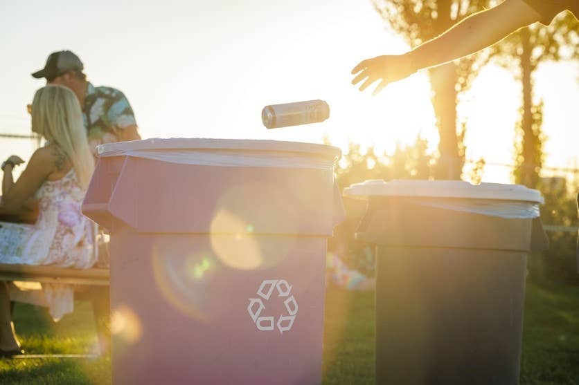 A fan throwing away an aluminum can in a recycling trash can.